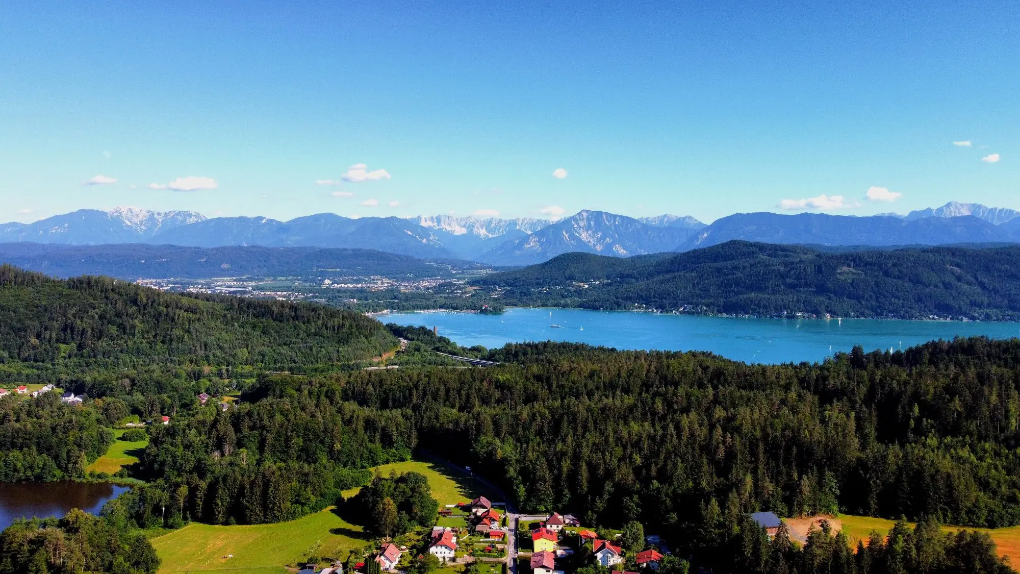 Blick von oben über einen Kärntner See zwischen Wäldern und Bergen